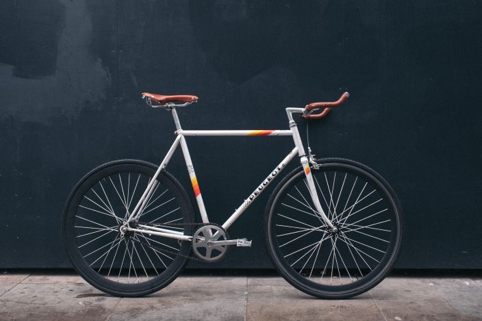 Gray fixie bike with orange highlights leaning on black wall